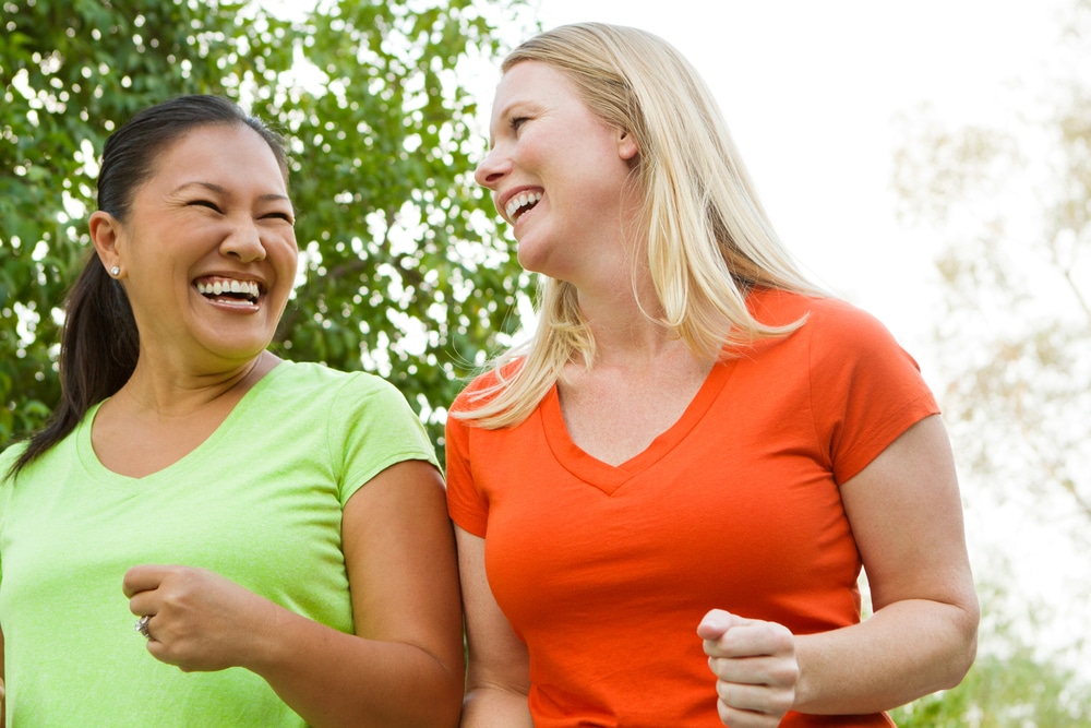 Two-women-laughing-together-as-they-walk-briskly-outdoors