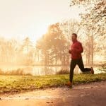 Man-in-jacket-running-outdoors-past-a-pond-at-sunrise