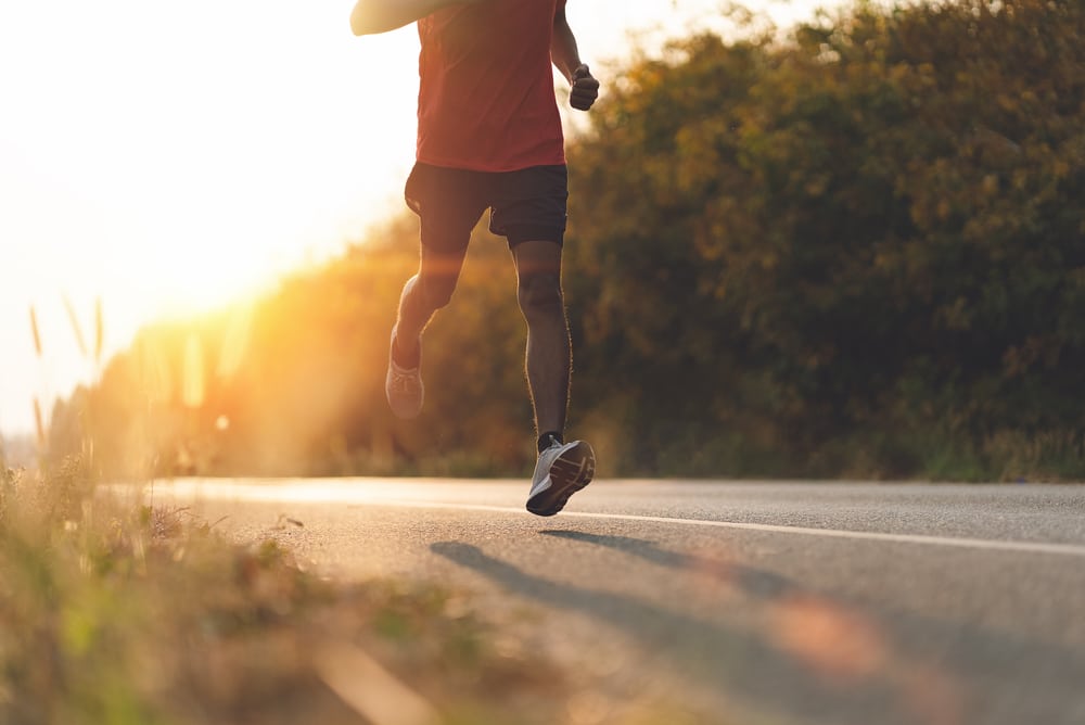 Man-in-mid-stride-running-down-side-of-tree-lined-highway