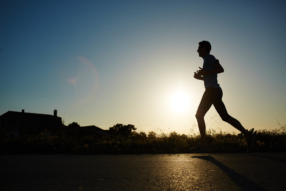 Man-jogging-along-country-road-at-sunset