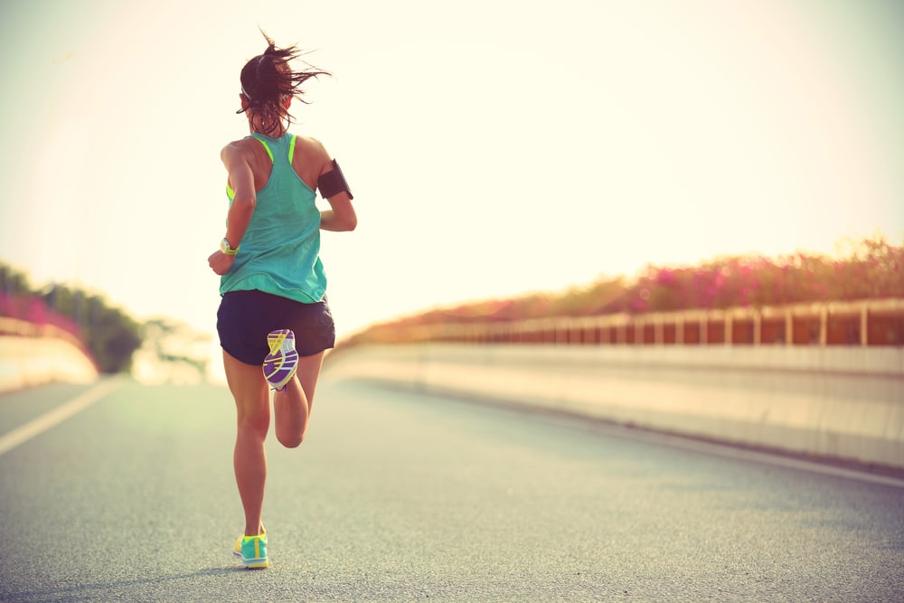 Woman-in-athletic-shorts-and-tank-top-running-down-paved-road-listening-to-headphones.