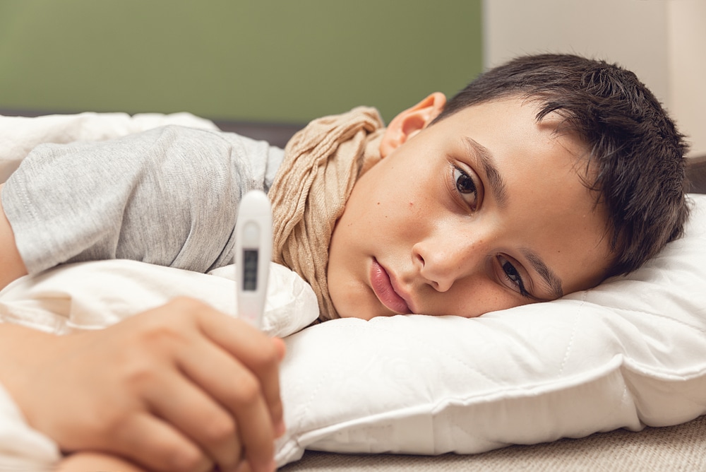 Sick boy lying in bed holding a thermometer