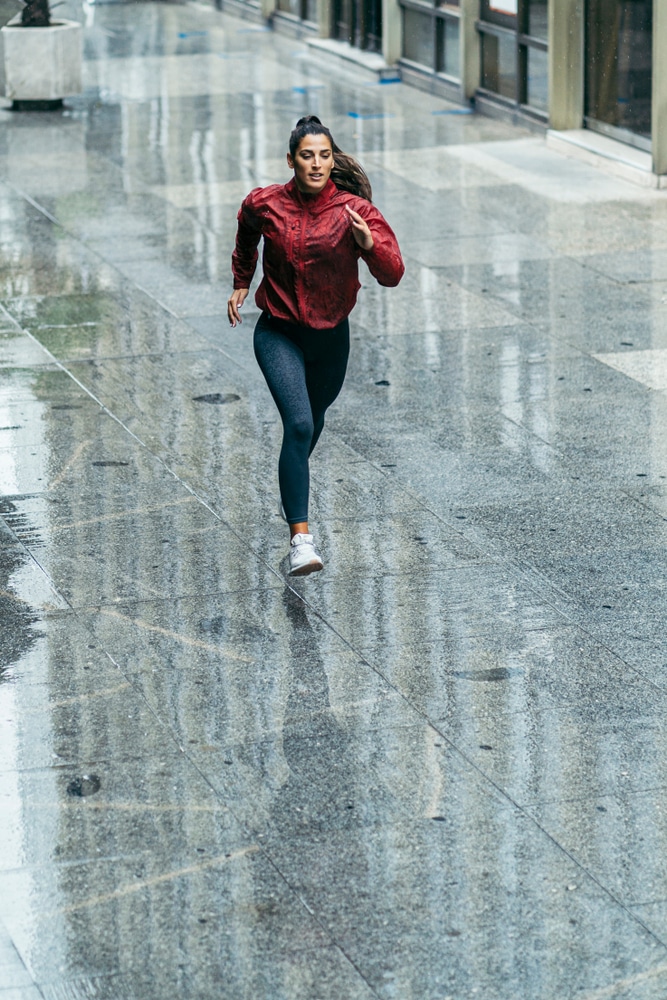 Woman in a red windbreaker running over a wet surface